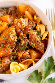 a white bowl filled with pasta and meat covered in sauce, garnished with parsley