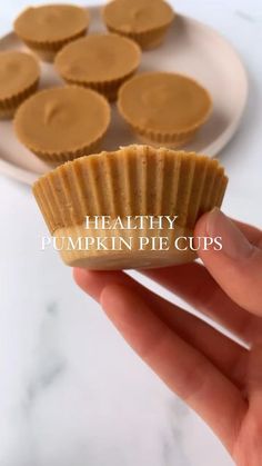 a hand holding a peanut butter cupcake in front of a plate with more muffins on it