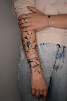 a woman with a tattoo on her arm holding onto another person's hand and wearing jeans