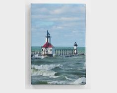 a lighthouse on the ocean with waves crashing in front of it and a pier behind it