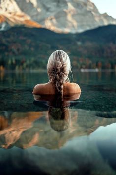 a woman sitting on top of a body of water with mountains in the back ground