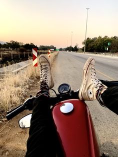 someone's feet on the handlebars of a red scooter in front of an empty road