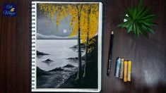 a notebook with an image of a lake and trees on it next to some crayons