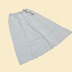 Vintage slip skirt (half slip), manufactured by Vanity Fair ca. 1980s. New old stock white lacy slip with original tags.     - Brand: Vanity Fair    - Size: Small (28"); see measurements    - Time Period: 1980s    - Color(s): White    - Materials: 100% cotton    - Made in: USA    - Condition: This piece of clothing is in new old stock vintage condition with original tags, with the only flaw being a minor pen mark which may be removable. Measurements (measurements taken lying flat; double for cir White Delicate Lace Skirt For Summer, Vintage Lace Trim Bottoms For Summer, Vintage Bottoms With Lace Trim For Summer, Vintage Bottoms For Summer Wedding, Summer Loungewear Slip With Lace Trim, Vintage White Lace Bottoms, Summer Slip With Lace Trim For Loungewear, White Vintage Lace Bottoms, White Lace Vintage Bottoms