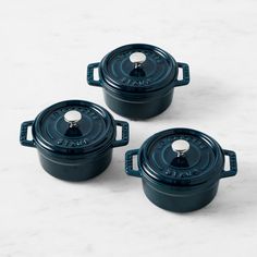 three blue cast iron casserole dishes on a marble surface