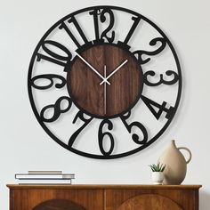 a clock that is on the wall next to a table with a vase and books