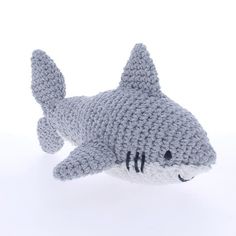 a crocheted stuffed shark toy laying on top of a white surface with its mouth open