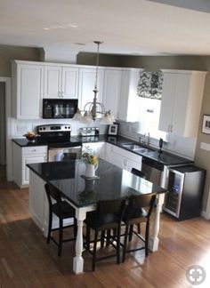 a kitchen with white cabinets, black counter tops and an island in front of the sink