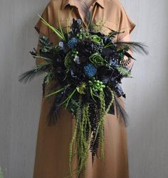 a woman wearing a brown dress holding a bouquet of black and green flowers in her hands