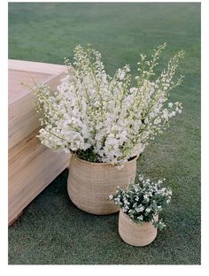 some white flowers are in a basket on the grass next to a wooden bench and planter