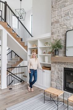 a woman standing in front of a fireplace next to a white book shelf with books on it