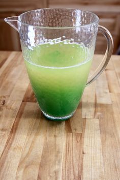 a pitcher filled with green liquid sitting on top of a wooden table