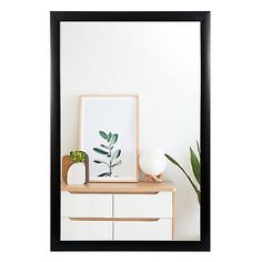 a white dresser with a black frame on it and a green plant in the corner