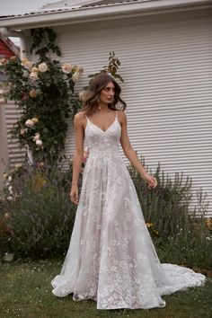 a woman standing in front of a white house wearing a wedding dress with an open back