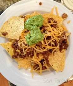 a white plate topped with nachos and guacamole next to tortilla chips