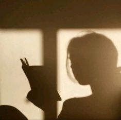 the shadow of a person holding a book in front of a window with light coming through it