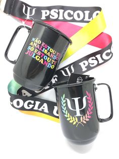 three black coffee mugs with colorful ribbons around them on a white background, one has a name tag and the other has a lanyard