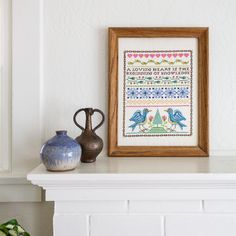 two vases and a framed cross - stitch pattern on a mantle