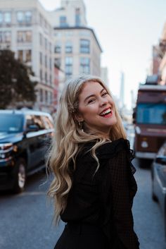 a woman with long blonde hair standing on the side of a road smiling at something