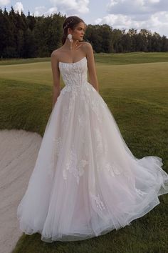 a woman in a wedding dress is standing on the grass near a golf course and trees