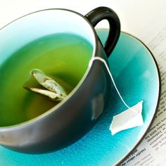 a tea cup filled with green liquid on top of a blue plate next to an open book