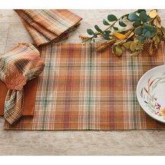 a place setting with plaid table cloths and fall leaves on the plate next to it