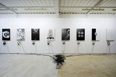 an art gallery with multiple black and white paintings on the wall, wires running through it