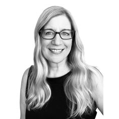 a black and white photo of a woman with long blonde hair wearing glasses smiling at the camera