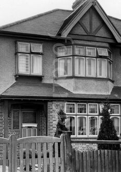 a black and white photo of a house with a wooden fence in front of it