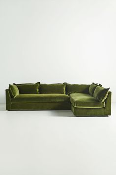 a large green couch with pillows on it's back and side, in front of a white wall