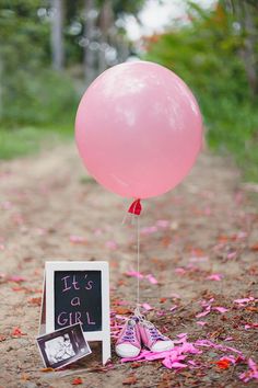 a pink balloon with a chalkboard attached to it sitting in the middle of a dirt road