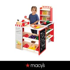 a young boy standing in front of a play kitchen with fruits and vegetables on it