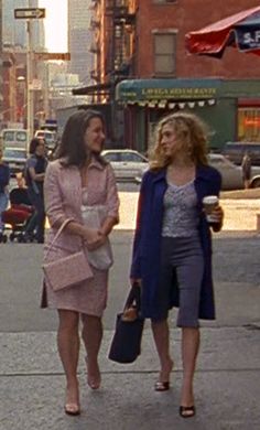 two women walking down the street talking to each other and one holding a purse in her hand