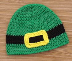 a crocheted green hat with black and yellow stitching on the front, sitting on top of a wooden surface