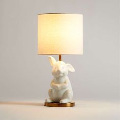 a small white rabbit lamp sitting on top of a table next to a light shade