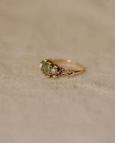 a gold ring with two green stones on the front and side, sitting on a white surface