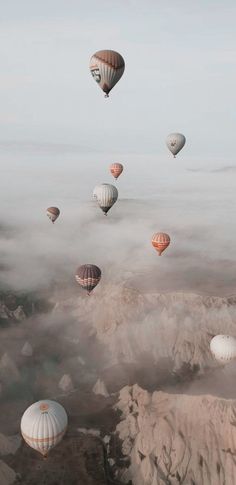 many hot air balloons flying in the sky above some mountains and clouds with low lying fog