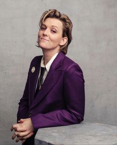 a woman in a purple suit sitting on top of a cement bench with her hands crossed