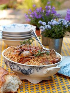 a bowl of food on a table with plates and flowers in the backround