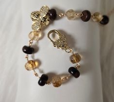 Float like a butterfly. Sting like a bee. The best of both worlds in this bracelet. The bee is a golden with pave cubic zirconia in white and black. The bee is offset to the side on this bracelet. The bracelet is secured pave CZ butterfly lobster clasp. The bracelet is handmade bead chain utilizing rich brown mahogany obsidian rondelles and citrines with 18 KT gold plated wire. The bracelet measures 7 inches and is adjustable up to 9 inches with the 18 KT gold plated chain with wire wrapped citrine rondelle. The gems are natural including any inclusions or flaws. I try to photograph creations as an accurate representation of the item. Gift Box included. Thanks for checking it out! Rondelle Mahogany Obsidian 8 MM x 5MM Citrine Rondelle 8MM x 5 MM 18 KT Gold Plated Pave CZ Butterfly Lobster Elegant Jewelry With Butterfly Charm And Round Beads, Brown Bracelet With Lobster Clasp As Gift, Elegant Brown Gemstone Beaded Bracelets, Brown Gemstone Bracelet As A Gift, Brown Gemstone Bracelet For Gift, Brown Gemstone Bracelet Gift, Elegant Brown Bracelet With Lobster Clasp, Brown Gemstone Bracelet Perfect For Gifts, Bee Bracelet