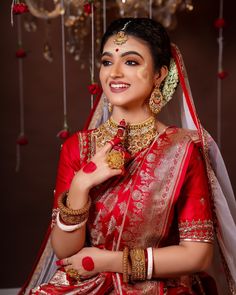 a woman in a red and gold bridal outfit posing for the camera with her hand on her shoulder