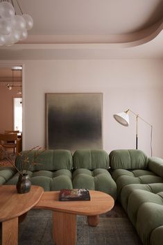 a living room filled with green couches and a wooden coffee table in front of a painting