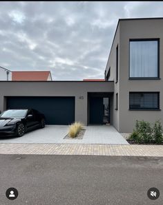 a black car parked in front of a grey two story house with garage doors and windows