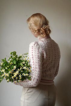 a woman holding a bouquet of daisies in her hands while standing against a wall