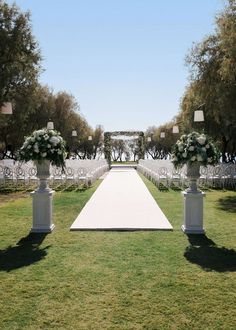 an outdoor ceremony setup with white flowers and greenery on the aisle, surrounded by trees