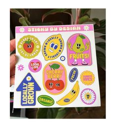 a sticker sheet with fruit and vegetables on it, in front of a potted plant