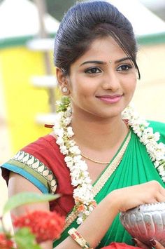 a woman in a green and red sari holding a silver vase with flowers around her neck