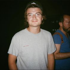 a man wearing glasses and a hat standing next to another man in a dark room