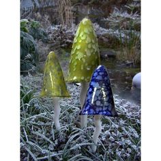 three glass mushrooms sitting on top of snow covered ground next to trees and bushes in the background