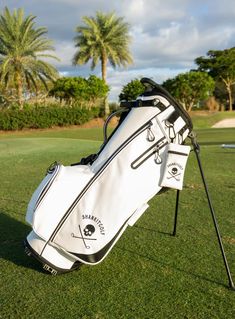 a white golf bag sitting on top of a green grass covered field with palm trees in the background